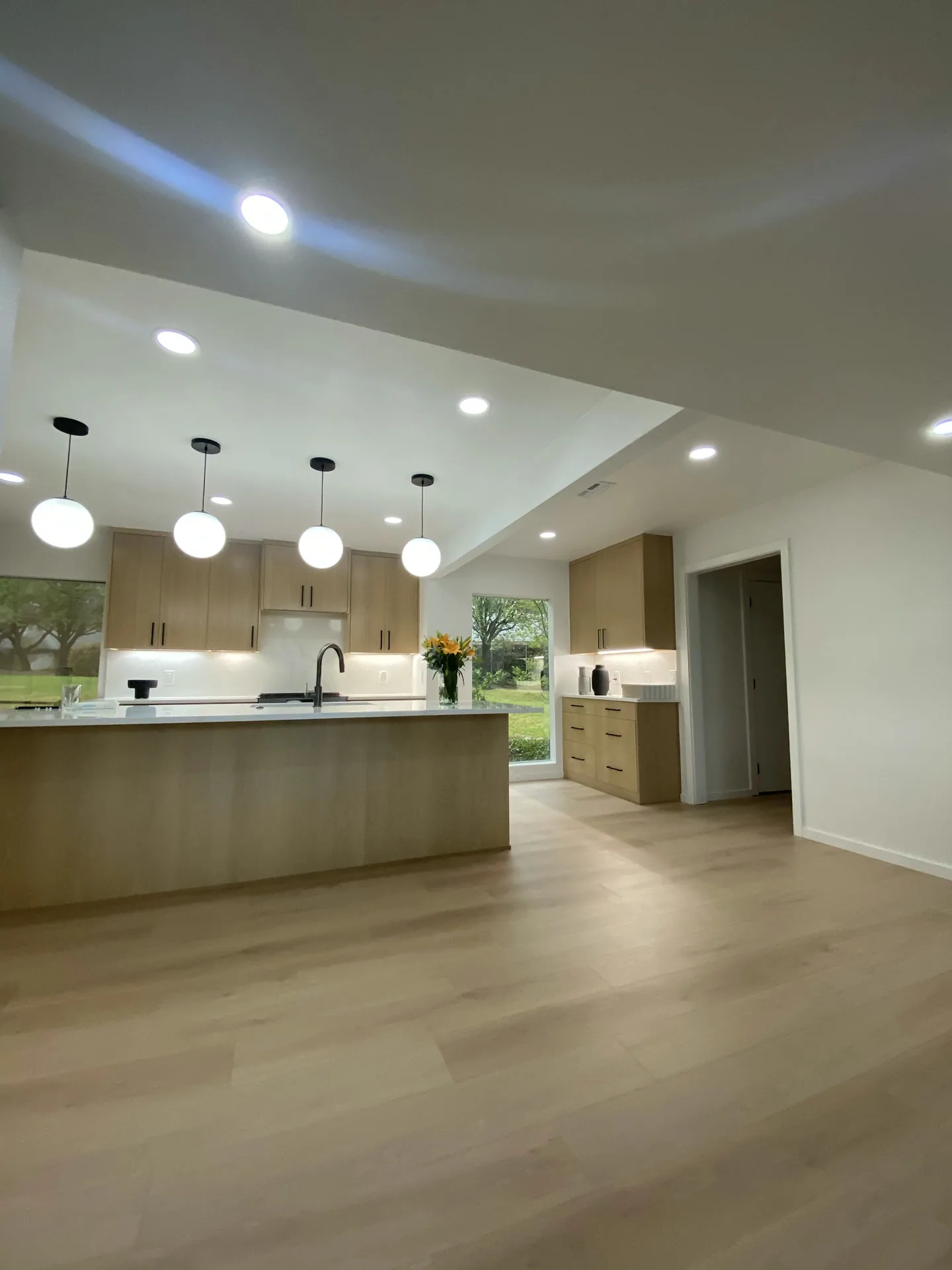 Kitchen with light wood-tone cabinets, white counters, flowers on the island and globe pendants